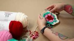 a woman is crocheting with yarn on the table next to a piece of paper