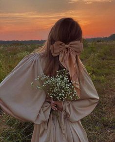 a woman standing in a field with her back to the camera holding a bouquet of flowers