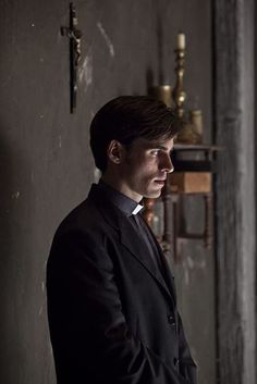 a man in a suit and tie standing next to a wall with candles on it