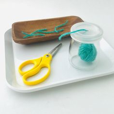 a pair of scissors sitting on top of a white tray next to a ball of yarn