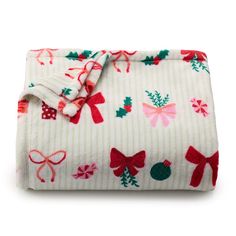 a white blanket with red bows and green leaves on the bottom is folded up in front of a white background