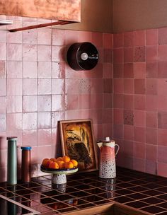 a pink tiled kitchen with oranges on the counter and a painting hanging above it