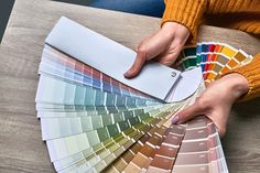 a person holding some paint samples on top of a wooden table with color swatches in front of them