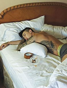 a shirtless man laying on top of a bed next to a cup and clock