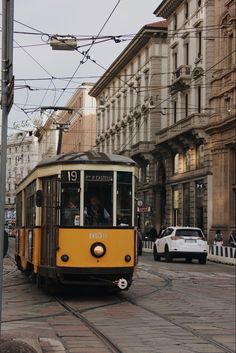 a yellow trolley car traveling down a street next to tall buildings