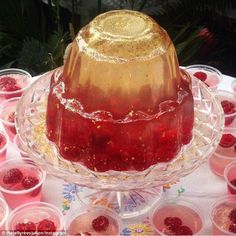 there is a cake on the table with many cups around it that have raspberries in them