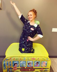 a woman standing on top of a toy bus with her hand up in the air