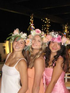 three girls wearing flower crowns standing next to each other in front of a building at night