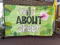 a sign that says wild about cheer hanging from the side of a building with flowers and leaves on it