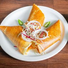 a white plate topped with three tacos covered in cheese and toppings on top of a wooden table