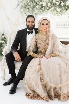 a bride and groom sitting on a white couch in front of a floral arch at their wedding