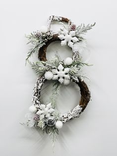 two wreaths with white flowers and greenery hanging on the wall