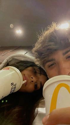 a man and woman drinking from cups in front of a mcdonald's sign at night