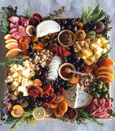 a platter filled with different types of cheeses, fruits and meats on top of each other