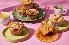 several muffins on plates next to two cups of coffee