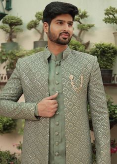 a man standing in front of a tree wearing a green suit and tie with an embroidered design on it