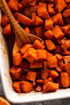 cooked sweet potatoes in a baking dish with a wooden spoon