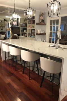 a kitchen island with four stools in front of it and lights hanging from the ceiling