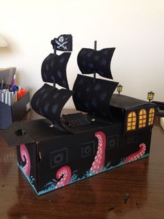 a pirate ship made out of cardboard sitting on top of a wooden table next to markers and pens