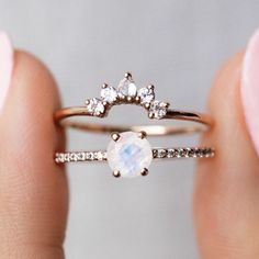 a woman's hand holding a ring with an oval white stone and diamond band