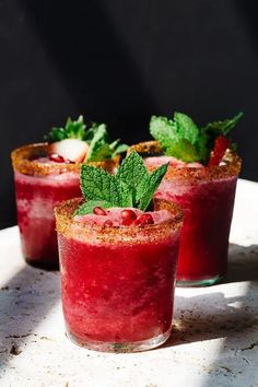 three glasses filled with different types of drinks on top of a white plate and topped with mint leaves