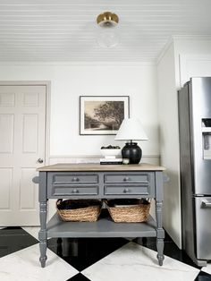 a kitchen island with two baskets on it in front of a refrigerator and a lamp