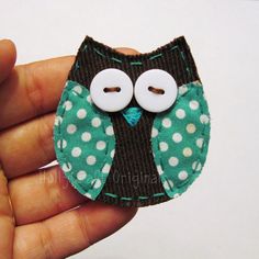 a hand holding a green and white owl brooch