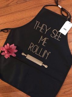 a black apron that says they see me rollin'with a pink flower on it