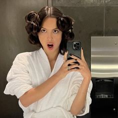 a woman taking a selfie in the bathroom with her hair pulled back and wearing a robe