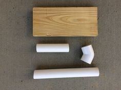 three pieces of wood and two white plastic objects on a gray carpeted floor with a wooden block in the background