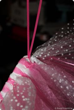 a pink umbrella with white polka dots hanging from it's side, in front of a dark background