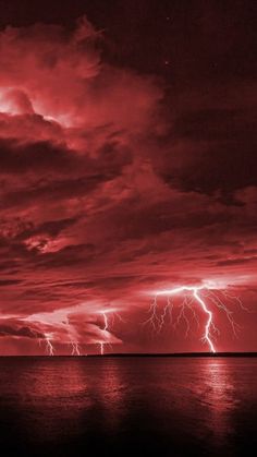 a red sky filled with lots of clouds and lightnings over the ocean at night