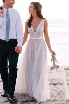 a man and woman are walking on the beach holding hands while dressed in formal attire