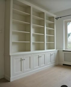 an empty room with white bookcases and wood flooring in front of a window