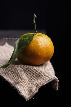 an orange sitting on top of a burlock with a leaf attached to it