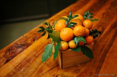 a wooden box filled with lots of oranges on top of a wood table and green leaves