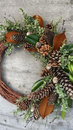 a wreath with pine cones, greenery and leaves on it sitting on a concrete surface