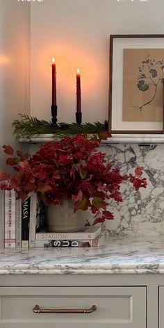 a vase with flowers on top of a counter next to two candles and some books