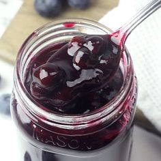 a glass jar filled with blueberries on top of a white table next to a spoon