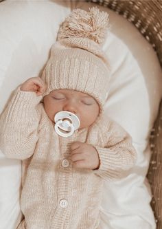 a baby in a knitted outfit is chewing on a pacifier while laying down