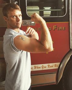 a man flexing his muscles in front of a fire truck