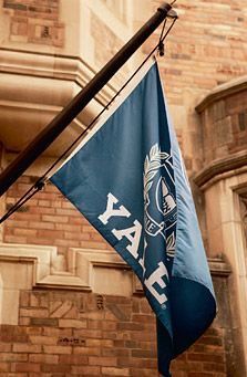 a flag hanging from the side of a building next to a tall brick building with a clock on it