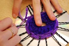 two hands are working on an ornament made out of yarn and cd disks