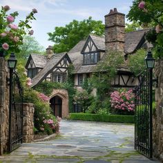 a stone walkway leading to a house with pink flowers in the front yard and an iron gate