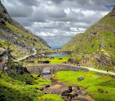 a scenic view of a valley with green grass, rocks and a road going through it