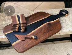 a wooden cutting board with black and brown handles sitting on top of a stone bench