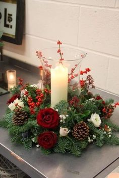 a candle is lit on a table with flowers and greenery in front of it