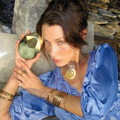 a woman in a blue dress is holding a vase with gold accents on her hands