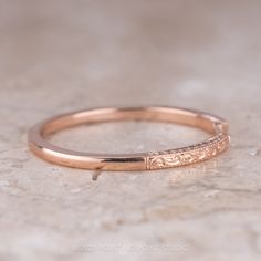 a rose gold wedding band with engraving on the side, sitting on a marble surface