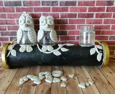 two owls sitting on top of a pipe next to some white rocks and a jar